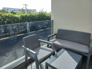 Ein Balkon mit einer Sitzecke aus einer Bank und zwei Stühlen, einer Glastrennwand und Blick auf eine Straße sowie auf Gebäude.