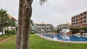 Ein Schwimmbecken mit Liegestühlen und Sonnenschirmen, umgeben von Grünflächen und mehrstöckigen Gebäuden.