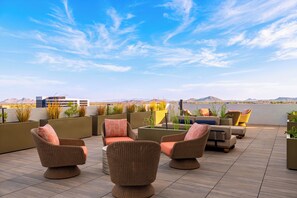 A rooftop terrace with wicker furniture, potted plants, and a view of the mountains. - Rooftop Pool + Gym + Sauna | Near TPC Golf + Preserve | Azur by AvantStay (Phoenix)