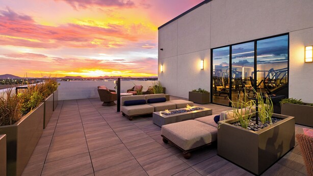 A rooftop terrace with seating, a fire feature, and a view of the sunset over the city.