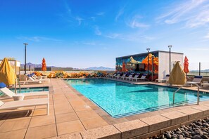 A pool area with lounge chairs, umbrellas, and a mural on the wall.