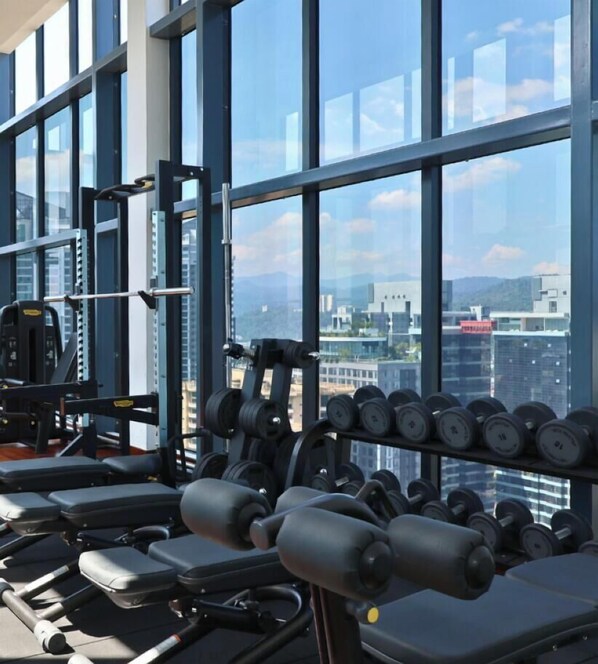 A gym with weightlifting equipment and dumbbells, large windows with a cityscape view. - Novo Ampang Suites By Asdeh (KL)