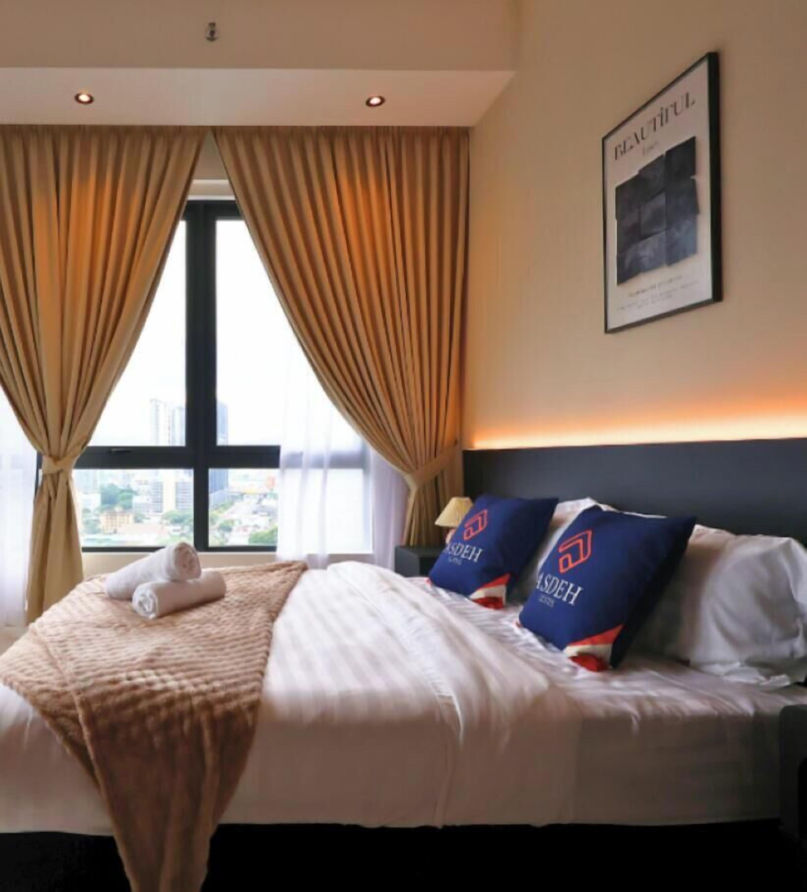 A hotel room with a bed, curtains, a pillow with a logo, a wall-mounted picture, and a window with a view.