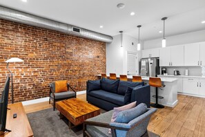A modern living room with a brick wall, a sofa, a coffee table, and a dining area with a kitchen in the background. - Stylish Downtown Nashville Condo • Near Broadway + Printer's Alley | Headliner (Nashville)
