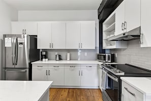 A modern kitchen with white cabinets, stainless steel appliances, and a wooden floor. - Stylish Downtown Nashville Condo • Near Broadway + Printer's Alley | Headliner (Nashville)