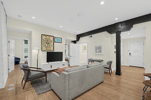 A modern living room with a grey sectional sofa, a flat-screen TV, and a dining area with a small table and chairs. - Brick + Full Kitchen | Half Block to Lower Broadway | Spotlight by AvantStay (Nashville)