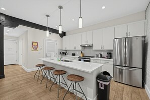A modern kitchen with white cabinets, stainless steel appliances, and a central island with bar stools. - Brick + Full Kitchen | Half Block to Lower Broadway | Spotlight by AvantStay (Nashville)