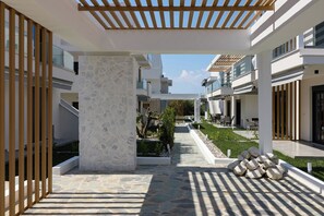 Un couloir extérieur moderne agrémenté d’un pilier en pierre, d’une pergola en bois et d’un espace détente avec des tables et des chaises.
