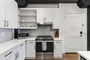 A modern kitchen with white cabinetry, a stainless steel oven, a microwave, and a black range hood. - Historic Loft + King Suite | 2-Min Walk to Honky-Tonks + Broadway | Showroom (Nashville)