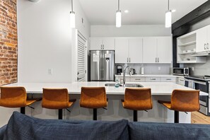 Una cocina moderna con armarios blancos, electrodomésticos de acero inoxidable y una isla central con taburetes de bar.