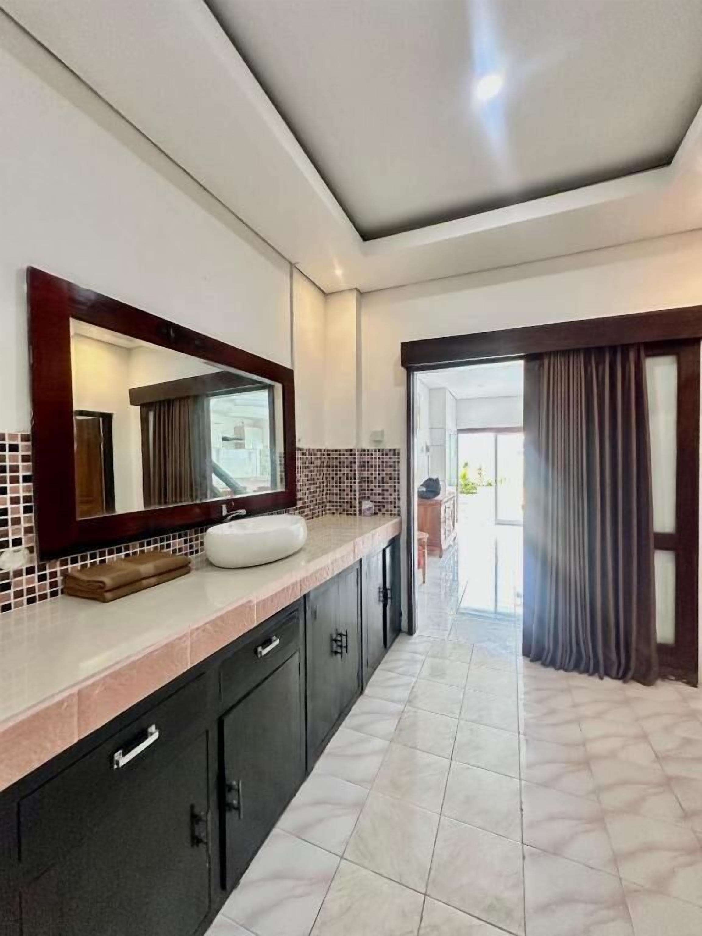 Une salle de bain moderne avec un grand miroir, des meubles sombres et un sol carrelé.