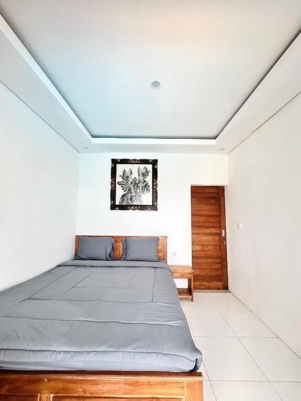 A bedroom with a bed, a nightstand, a wooden door, and a framed picture on the wall.