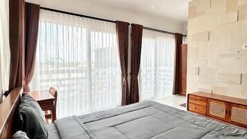 Habitación de hotel con una cama grande, cabecera de madera, cómoda de madera y vistas a través de cortinas traslúcidas.