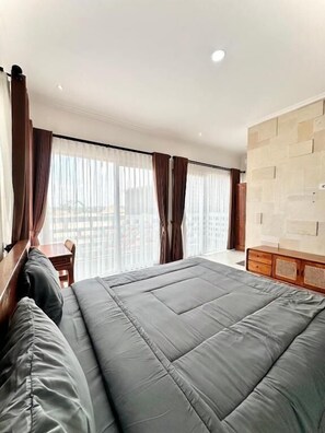 A hotel room with a large bed, a wooden headboard, a wooden dresser, and a view through sheer curtains. - Kailash Suites Balangan (Jimbaran)