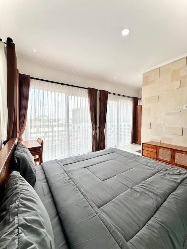 A hotel room with a large bed, a wooden headboard, a wooden dresser, and a view through sheer curtains. - Kailash Suites Balangan (Jimbaran)