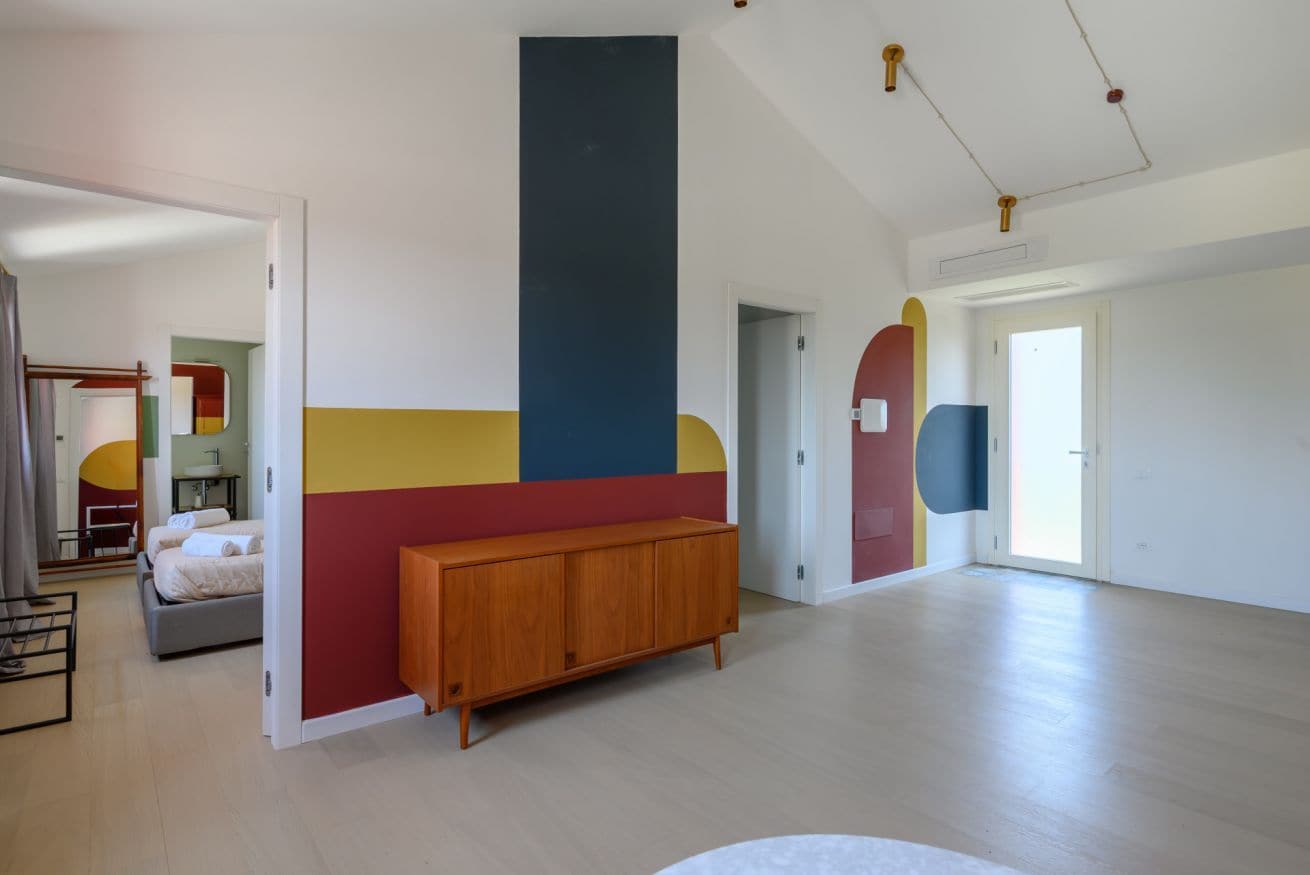 A modern hotel room with a large bed, a wooden bench, and a colorful wall design.