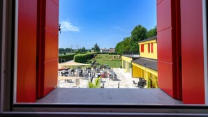 Ein offenes Fenster mit Blick auf einen Innenhof, der Sitzgelegenheiten im Freien und ein gelbes Gebäude im Hintergrund bietet.