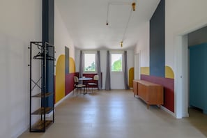 Een gang met een houten vloer, een metalen rek, een tafel met stoelen en een kast.