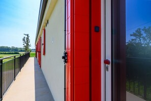 A corridor with red doors, a black railing, and a view of a green landscape. - GuestHost - Kidane Apartment Padova (Padua)