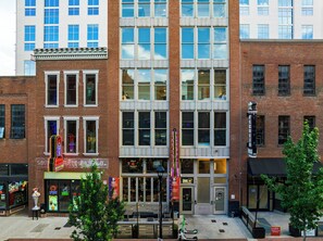 A multi-story building with a brick facade, large windows, and a storefront with illuminated signage. - Group-Friendly Condo + King Suite | Steps to Music Hall + Broadway | Mic Drop (Nashville)