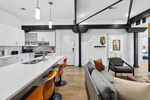 Uma cozinha moderna com uma ilha central, banquetas e uma área de jantar com sofá e cadeiras.