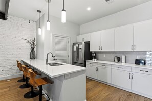 A modern kitchen with white cabinetry, a stainless steel refrigerator, a built-in oven, and a bar area with stools. - Group-Friendly Condo + King Suite | Steps to Music Hall + Broadway | Mic Drop (Nashville)