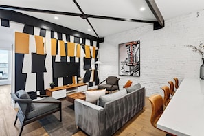 A modern living room with a sectional sofa, a coffee table, and a TV. - Group-Friendly Condo + King Suite | Steps to Music Hall + Broadway | Mic Drop (Nashville)