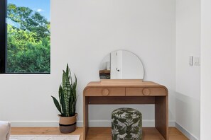 A minimalist room with a wooden vanity, a mirror, a potted plant, and a small stool. - Plunge Pool + Firepit + Skyline Deck | Steps to SoCo | Elizabeth House (Austin)