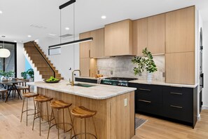 A modern kitchen with a central island, bar stools, a stove, and wooden cabinetry. - Plunge Pool + Firepit + Skyline Deck | Steps to SoCo | Elizabeth House (Austin)