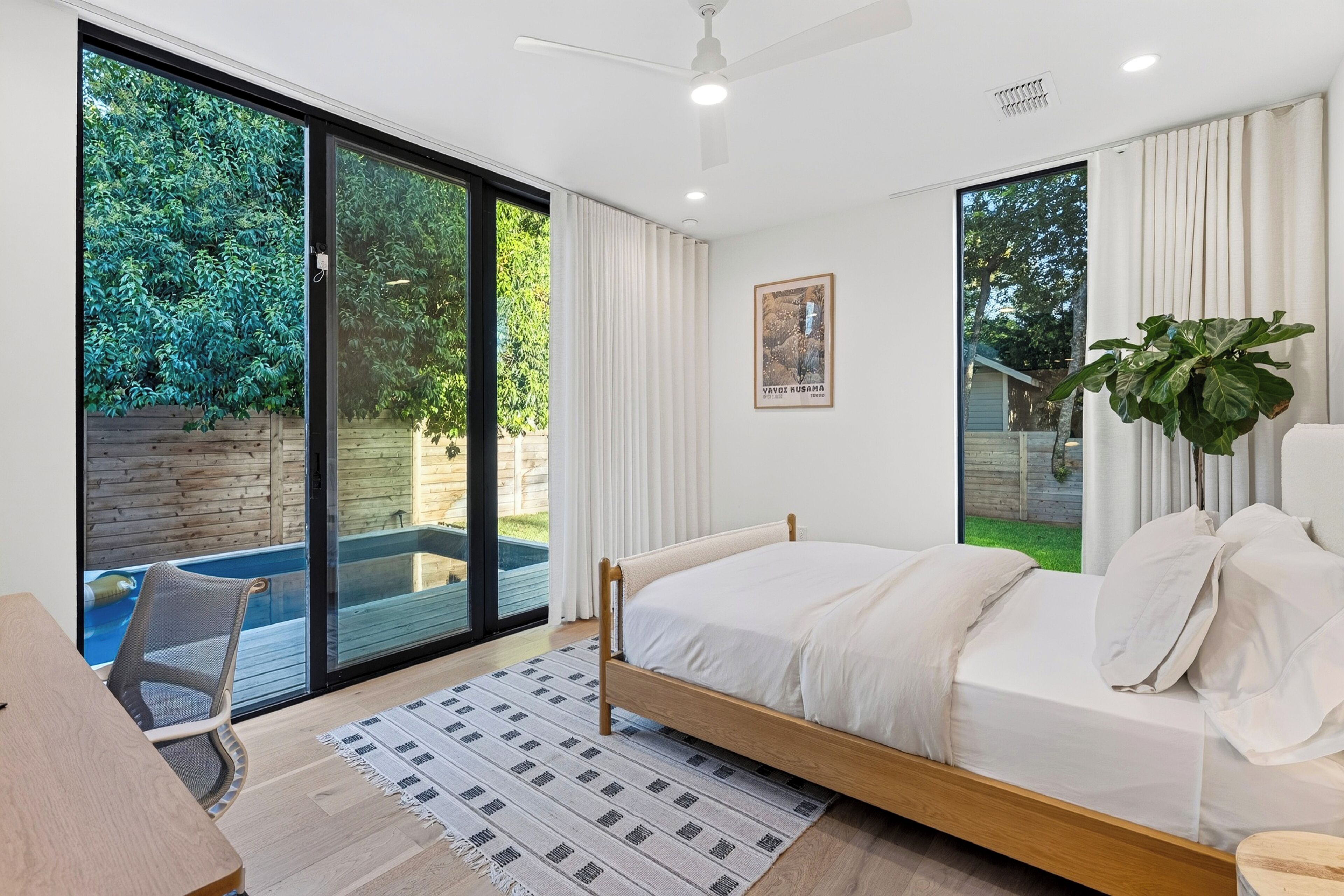 Un dormitorio moderno con una cama grande, un escritorio y vistas a una piscina y jardín.