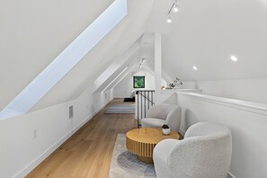 Una camera da letto mansardata moderna con un lucernario, pavimento in legno, un tavolino rotondo e un divano grigio.