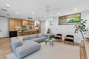 Una sala moderna con un sofá seccional gris, una mesa de centro de vidrio y dos sillas de madera.