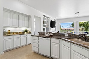 A modern kitchen with white cabinetry, granite countertops, and a built-in TV. - Golf Views + BBQ Patio | Mins to Indian Wells | Palm & Par (Palm Desert)