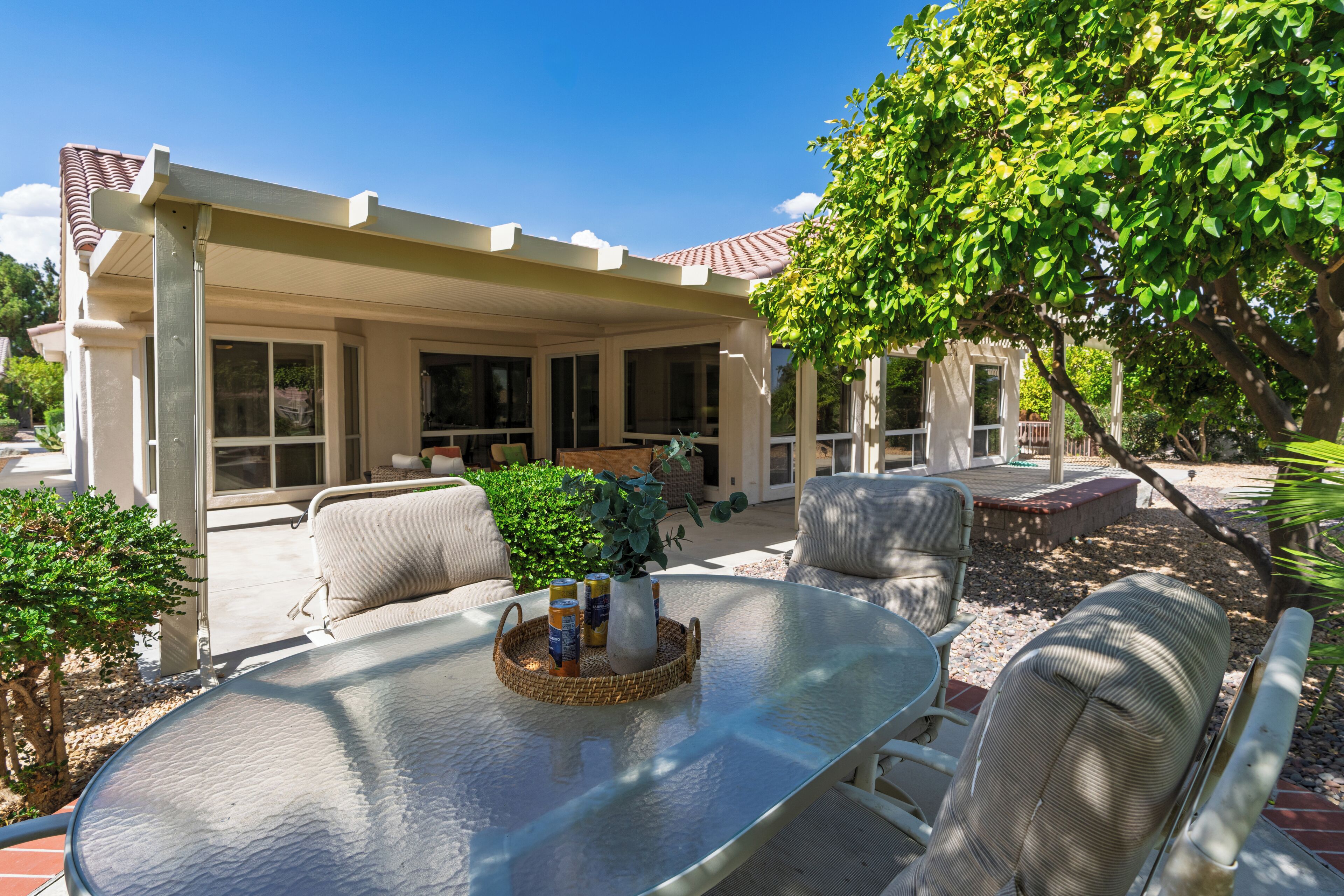 A covered patio area with outdoor furniture, including a glass-top table and chairs, and a pergola structure.