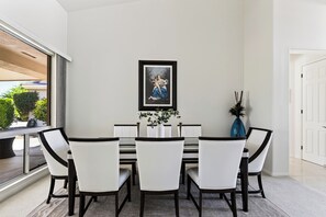 Un coin repas avec une table blanche, des chaises noires et une œuvre d’art encadrée au mur.