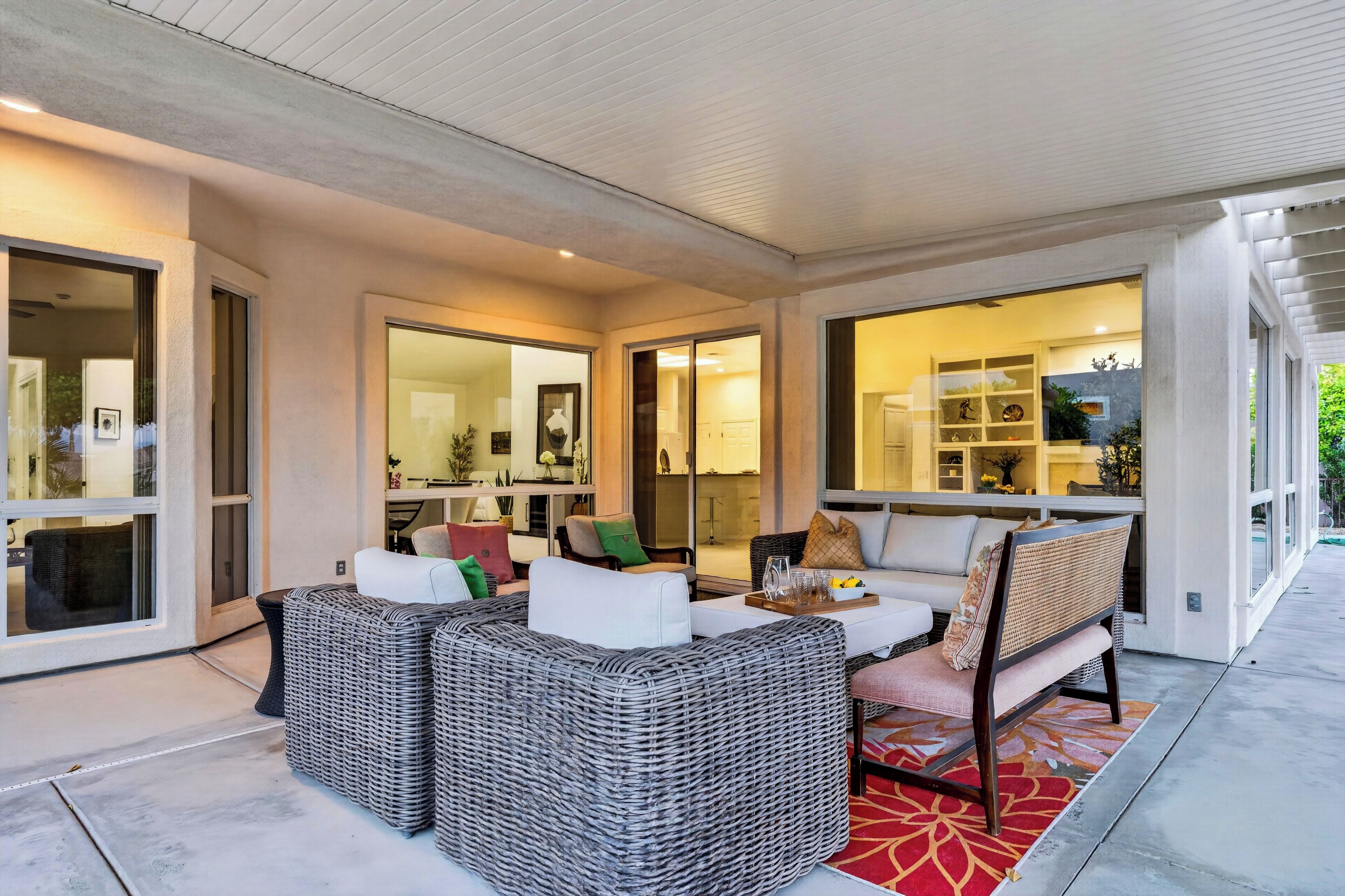 A modern outdoor living area with wicker furniture, a glass-enclosed kitchen, and a view of the surrounding landscape.
