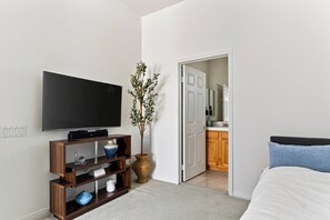 A bedroom with a television, a plant, and a door leading to a bathroom. - Golf Views + BBQ Patio | Mins to Indian Wells | Palm & Par (Palm Desert)