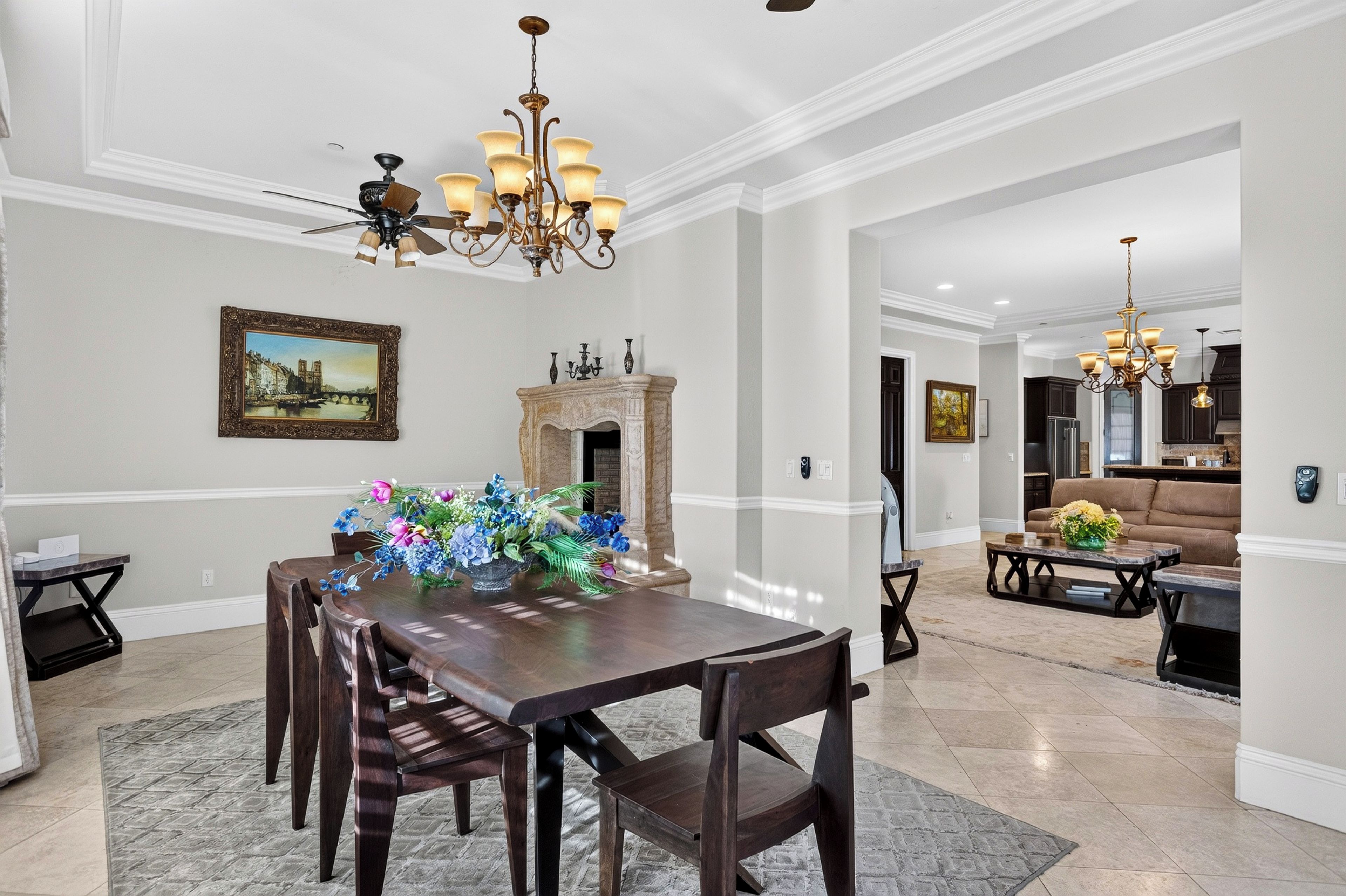 A dining area with a long wooden table, chairs, a chandelier, a fireplace, and a painting on the wall.