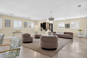 A spacious living room with a beige carpet, a chandelier, and a large sofa. - 20 Acres • Lake + Pool + Spa • Near Hard Rock Casino | Vista del Lago Estate (Bakersfield)