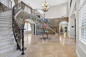 A grand staircase with ornate metal railings, a chandelier, and a floral centerpiece on a round table. - 20 Acres • Lake + Pool + Spa • Near Hard Rock Casino | Vista del Lago Estate (Bakersfield)