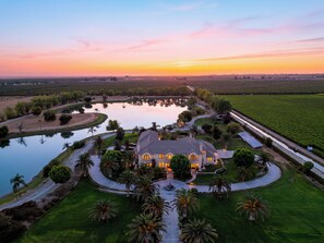 A large estate with a central building surrounded by a lake, pathways, and palm trees. - 20 Acres • Lake + Pool + Spa • Near Hard Rock Casino | Vista del Lago Estate (Bakersfield)