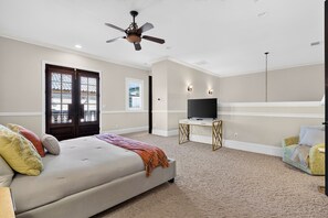 A bedroom with a bed, a television on a stand, a ceiling fan, and a door with a view to the outside. - 20 Acres • Lake + Pool + Spa • Near Hard Rock Casino | Vista del Lago Estate (Bakersfield)