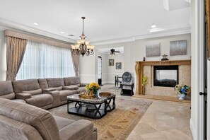 A spacious living room with a large sofa, a coffee table with decorative items, a fireplace, and a ceiling fan. - 20 Acres • Lake + Pool + Spa • Near Hard Rock Casino | Vista del Lago Estate (Bakersfield)
