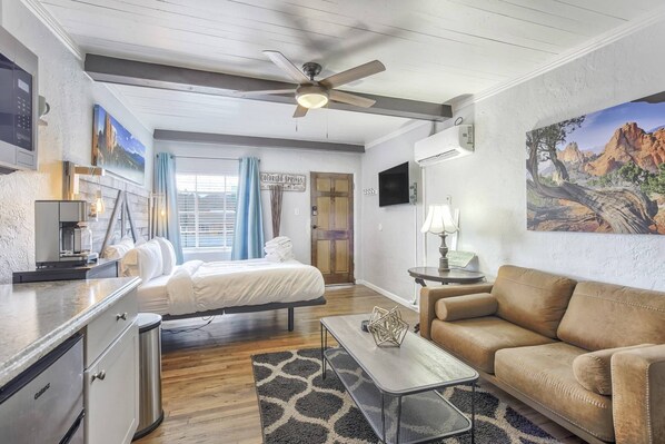 A hotel room with a bed, a sofa, a coffee table, a TV, and a painting.