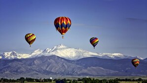 Eine Landschaft mit vier Heißluftballons über einem verschneiten Gebirgszug.