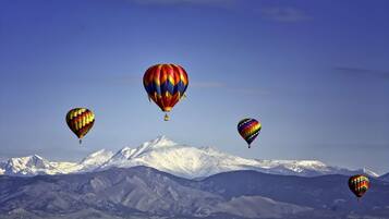 A landscape with four hot air balloons flying over a snow-capped mountain range.