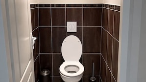 A modern bathroom with a toilet, a trash bin, and a hanging light fixture.