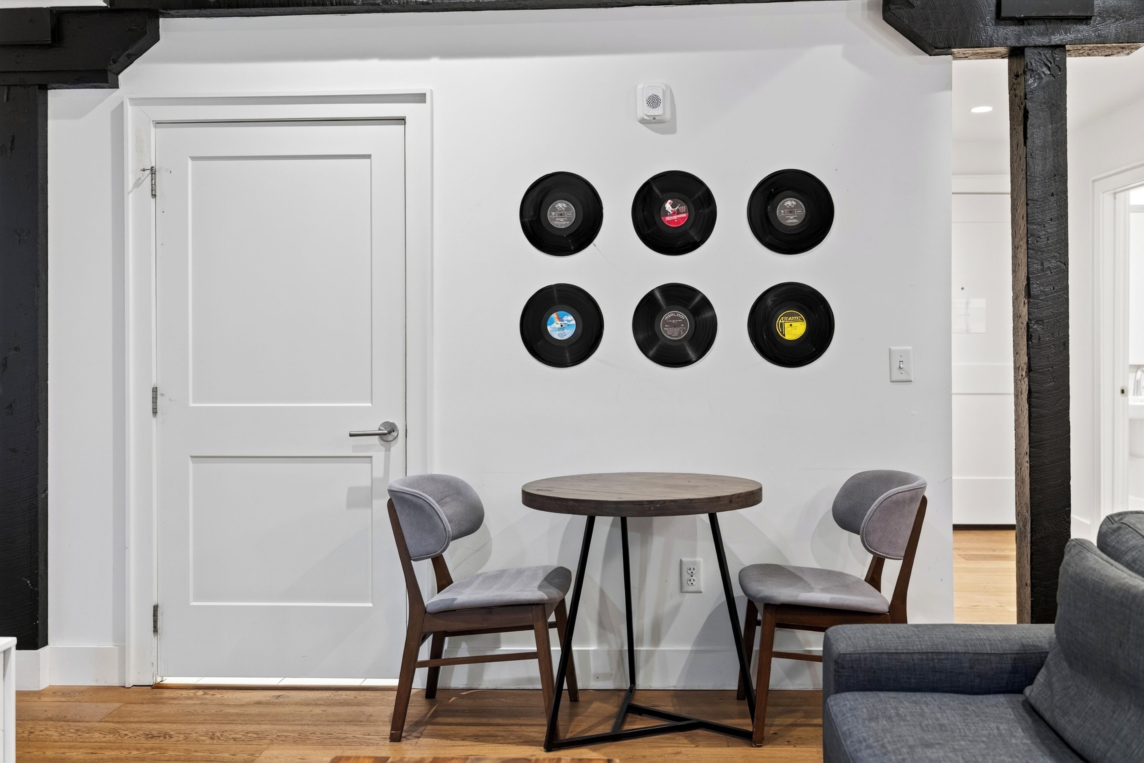 Una habitación con una puerta blanca, una mesa redonda con dos sillas y una pared con seis discos de vinilo.