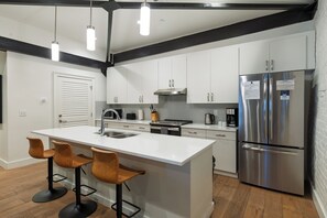 A modern kitchen with white cabinetry, stainless steel appliances, and a central island with bar stools. - King Suite + Full Kitchen | Steps to the Honky-Tonks + Broadway | The Vault (Nashville)