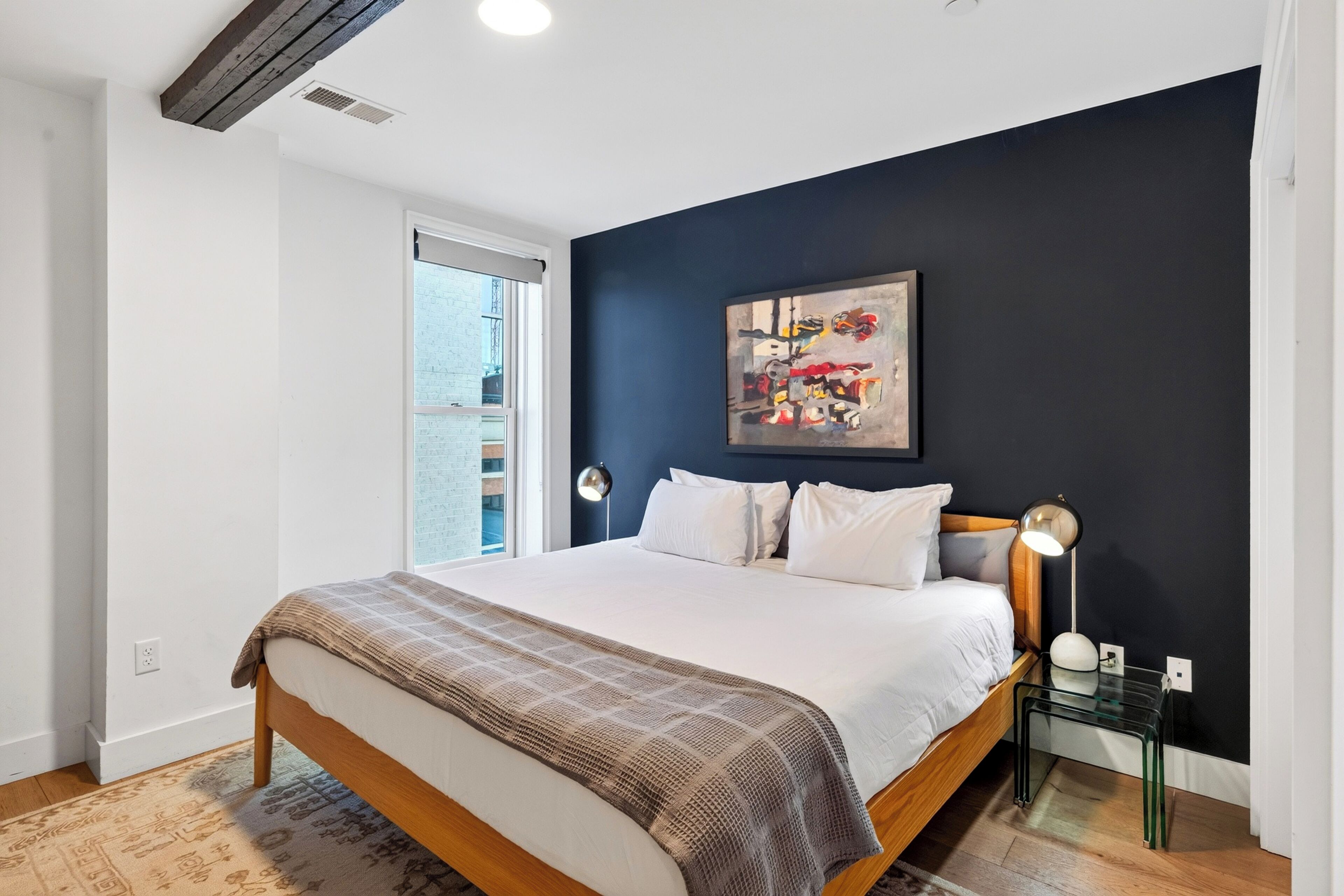 A bedroom with a bed, a nightstand, a lamp, and a painting on the wall.